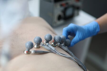Close-up of clinical worker stick special equipment to mans chest for ecg test. Macro shot of...