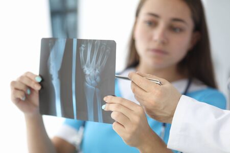 Close-up of surgeon hands holding wrist skiagram. Serious woman in medical uniform consulting with...