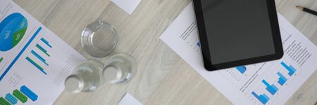 Top view of documents with financial statistics. Turned off tablet on working desk. Papers with...