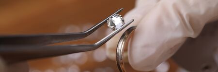 Close-up of goldsmith hand decorating precious ring with beautiful diamonds. Professional jeweler using special equipment. Gold jewelry production conceptの写真素材