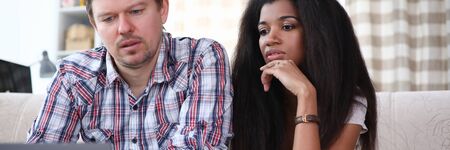 Portrait of concentrated family surfing something via internet app on laptop. Man and woman sitting in comfortable room. People looking at screen seriouslyの写真素材