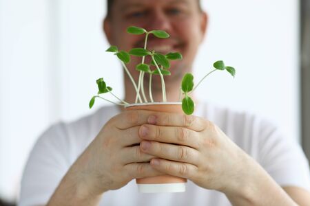 Close-up of happy middle-aged man holding paper coffee cup as pot for flower. Smiling male and green plant. Agriculture and growth. Spare time and hobby conceptの写真素材