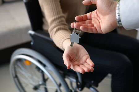 Close-up of realtor putting keys from new apartment on owners hand. Person sitting in wheelchair. Disabled people. Buy property. Real estate and mortgage conceptの写真素材