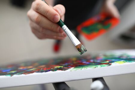 Top view of person creating new masterpiece. Mans hand holding brush and applying colour on canvas. Fresh idea for painting. Hobby for soul and creativity conceptの写真素材