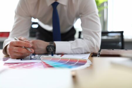 Close-up of man in stylish suit holding silver pen. Male person in office. Creative designer and architect. Colourful samples palette. House renovation and new interior conceptの写真素材
