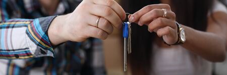 Focus on people hands holding keys of new apartment. Man and woman smiling and looking happy about...