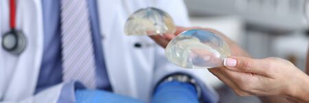 Close-up of female hands holding silicone implants in hands. Plastic surgeon in medical gown...