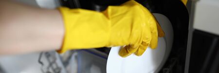 Hands in gloves put plate to dishes in dishwasher. Features washing dishes in an automated way. Use dishwashers in apartment. Equipment high-quality dishwashing does not require lot timeの写真素材