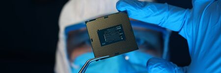 Man in uniform holds microprocessor with forceps. Software-controlled device for processing...