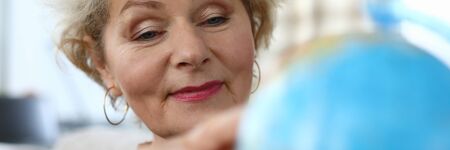 Grandmother looks at globe at home and dreams trip. An elderly woman is considering map states...