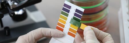 Hands holding litmus test paper for soil analysis. Litmus paper shows acidity, chemical analysis....