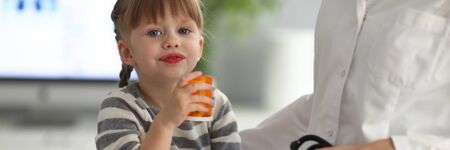Portrait of happy little patient looking at camera with happiness. Smiling girl holding bottle with medication. Child taking vitamins. Healthcare and prevention conceptの写真素材