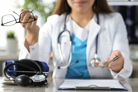 Close-up of therapist hands holding glasses and pen. Tonometer and documents on table. Doctor office...