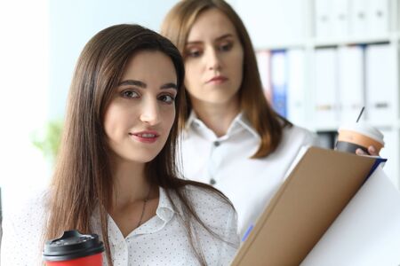 Portrait of pretty businesswoman holding important tablet with biz documents and working with smart friendly female colleague. Accounting office conceptの写真素材