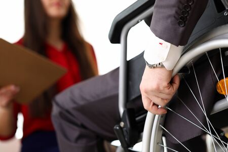 Man in suit on wheelchair communicates with woman. Prestigious job for people with disabilities. Office has working conditions for disabled. Active employment people with disabilitiesの写真素材