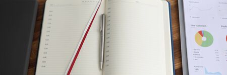 Daily planner, keyboard on desk company employee. Responsible worker table. On it stapler, closed notebook, book with graphs for time and schedule for day, computer, clipboard with other documents.の写真素材