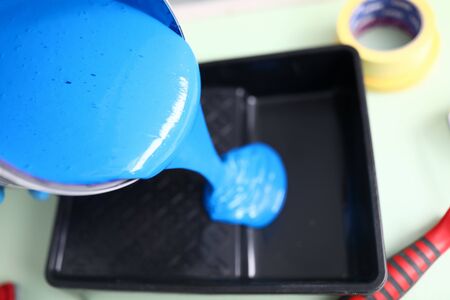 Top view of person pouring blue paint for painting wall in apartment. Black plastic container for renovation material. Construction site and interior design conceptの写真素材