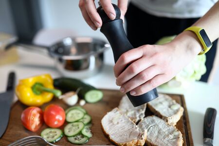 Close-up of woman using pepper for slices of meat. Yellow sweet pepper cucumber and tomato on wooden...