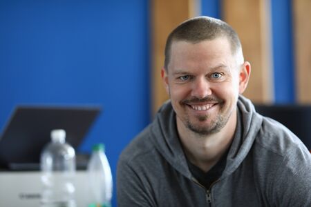Portrait of smiling cheerful middle-aged male posing on camera indoors. Happy person wearing grey hoodie. Copy space in left side. Modeling and happiness conceptの写真素材