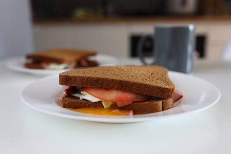 Close-up of delicious sandwich made of bread tomato cheese butter and sausage. Tasty lunch or breakfast. Fast food and quick snack for tea or coffee conceptの写真素材