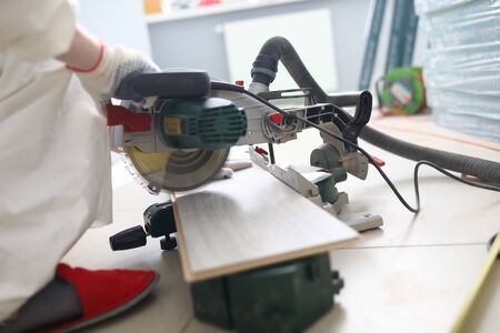 Close-up of male worker holding electrical equipment for drill. Silver colour of instrument. Man in protective costume cutting laminate. Renovation and construction site conceptの写真素材
