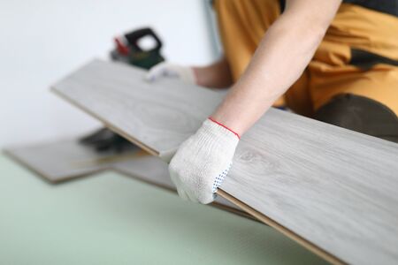 Close-up of professional craftsman holding luxury grey wooden laminate. Male worker in yellow uniform and white gloves. Renovation and construction site conceptの写真素材
