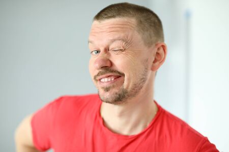 Portrait of funny cute man posing on camera. Joyful person making faces. Mature middle-aged male in red tshirt. Adult winking standing indoors. Modern conceptの写真素材