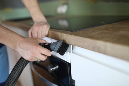 Close-up of man from professional cleaning service clean kitchen furniture with vacuum cleaner....