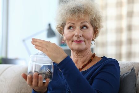 Portrait of senior charming woman holding glass container for money. Elderly female and piggy bank...