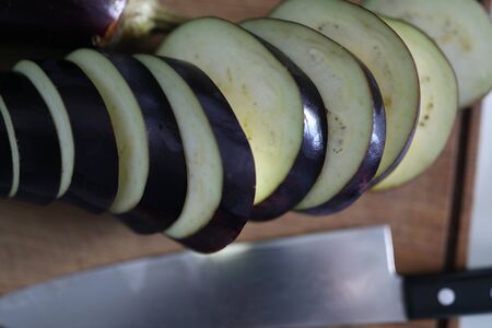 Cut organic eggplant and knife on kitchen table. Cooking in quarantine and self-isolation. Healthy vegetable recipes. Cooking and eating at home. Search for inspiration and new recipesの写真素材