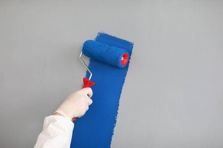 Male painter in uniform paints wall with roller. Professional uses simple hand tool. Paint large...