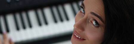 Woman turns around while playing electronic piano. Musician tunes sound on electronic piano to record composition. Student gets used to musical instrument, learns to play colorful keysの写真素材