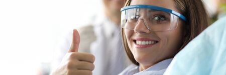 Visit to dentist, girl in clinic shows gesture ok. Dentist conducts full examination teeth, gums and oral cavity in search signs disease or other problems. Patient is pleased with work doctor.の写真素材