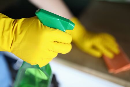 Close-up of person using cleaning product and wearing bright yellow gloves. Male holding rag....