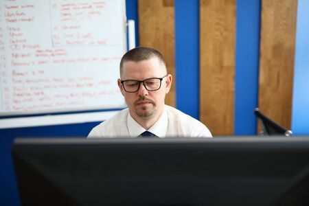 Portrait of concentrated male programmer sitting in stylish office. Smart man working on modern...