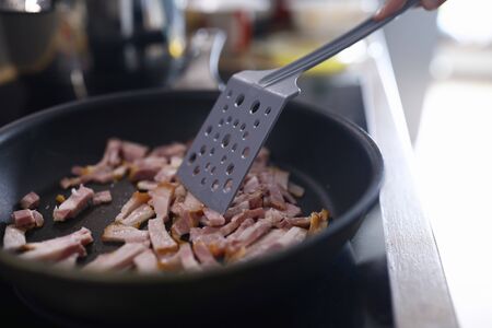 Close-up of female frying small slices of bacon on pan. Woman cooking tasty dinner or breakfast for family. Juicy and fresh meat with oil. Unhealthy nutrition conceptの写真素材