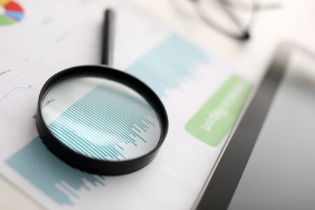 Close-up of black magnifying glass laying on paper with diagram. Equipment for better examine documents. Tablet on table. Business and successful financial company conceptの写真素材