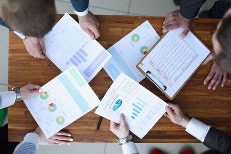 Top view of smart business people discuss important question in office. Papers with charts and...