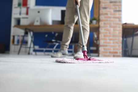 Low angle of man cleaning floor at home with rag. Grey ground in apartment. Tool for cleanliness. Cleaning service and supplies. Renovation and interior design conceptの写真素材