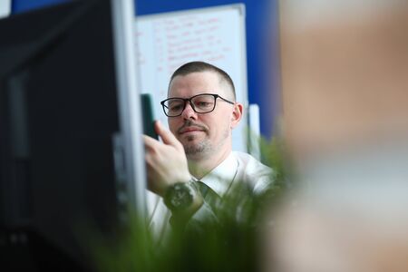 Portrait of businessman sitting in office and using smartphone. Man in stylish black glasses with...