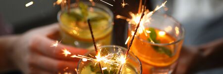 Young group friends hold in hand fruit cocktail with sparkler decoration. Christmas invite party concept. Heath care vegan summer drinksの写真素材