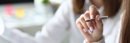 Focus on gentle arm of hardworking woman manager sitting at modern workplace and holding metallic writing pen and discussing something with colleague. Accounting office conceptの写真素材