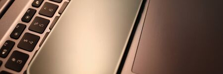 Silver smartphone lie on laptop keyboard in office close-up. Business education concept