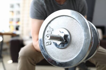 Close-up of male person lifting heavy metal dumbbell sitting on chair. Strong fit body. Training and exercise for best result. Home gym and active lifestyle conceptの写真素材