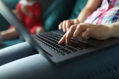 Close-up of persons hand working on laptop sitting on cozy sofa. Young female typing on grey modern device. Freelancer on quarantine period. Technology and remote job from home conceptの写真素材