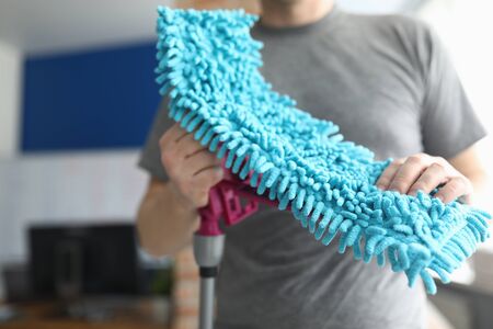 Close-up of male person holding fluffy blue rag for floor cleaning. Equipment for wet clean. Cleaning service. Dust on apartment furniture. Househusband and purity conceptの写真素材