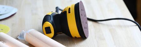 Close-up of bright sander machine laying on wooden table. Papers with plan of renovation. Working place with polishing equipment. Construction site and technology conceptの写真素材