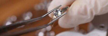 Close-up view of persons hands in protective gloves holding special equipment and examining quality of diamond. Magnifying loupe on table. Luxury jewelry conceptの写真素材