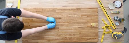 Top view of construction worker polishing wood. Male in protective gloves. Tools and sander machine on other side of table. Renovation and carpenter job conceptの写真素材