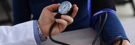 Close-up of doctor hands holding tonometer and measuring pressure to ill patient. Therapist making...